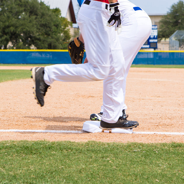 Baseball player in white uniform with black shoes on a baseball field stepping on a Champion 15" X 15" Foam Filled Quilted Cover Base