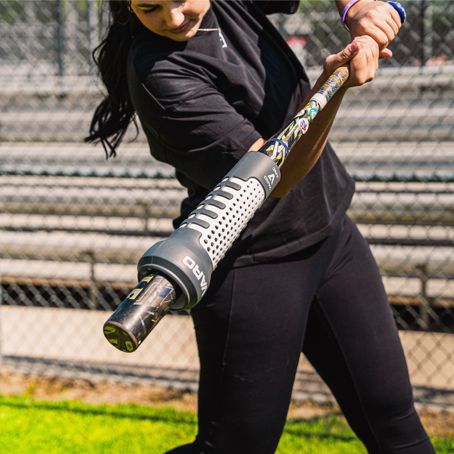 Person holding a baseball bat with Varo ARC Bat Weight 12 Oz on it, on a sports field with blurred background