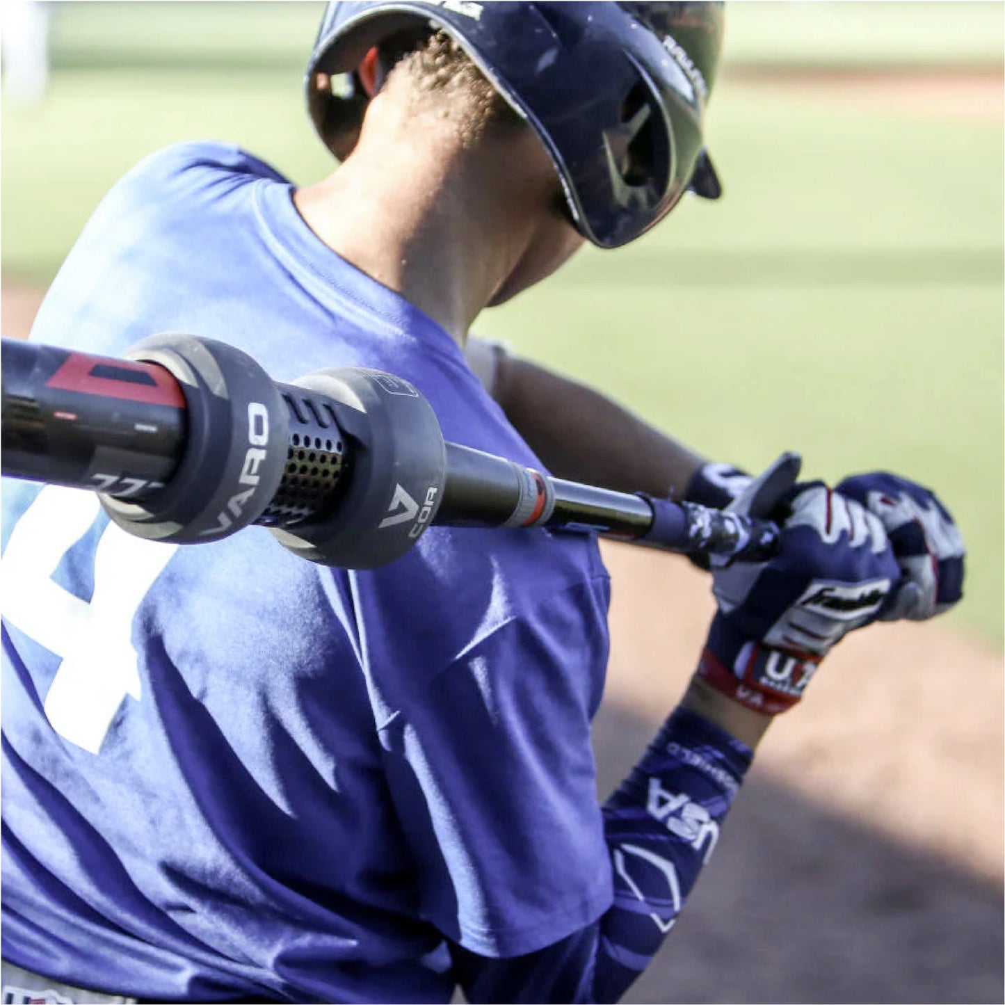 Baseball player in blue uniform with a bat with Varo COR Bat Training Weight 24oz attached on it, wearing a helmet and gloves, on a field.