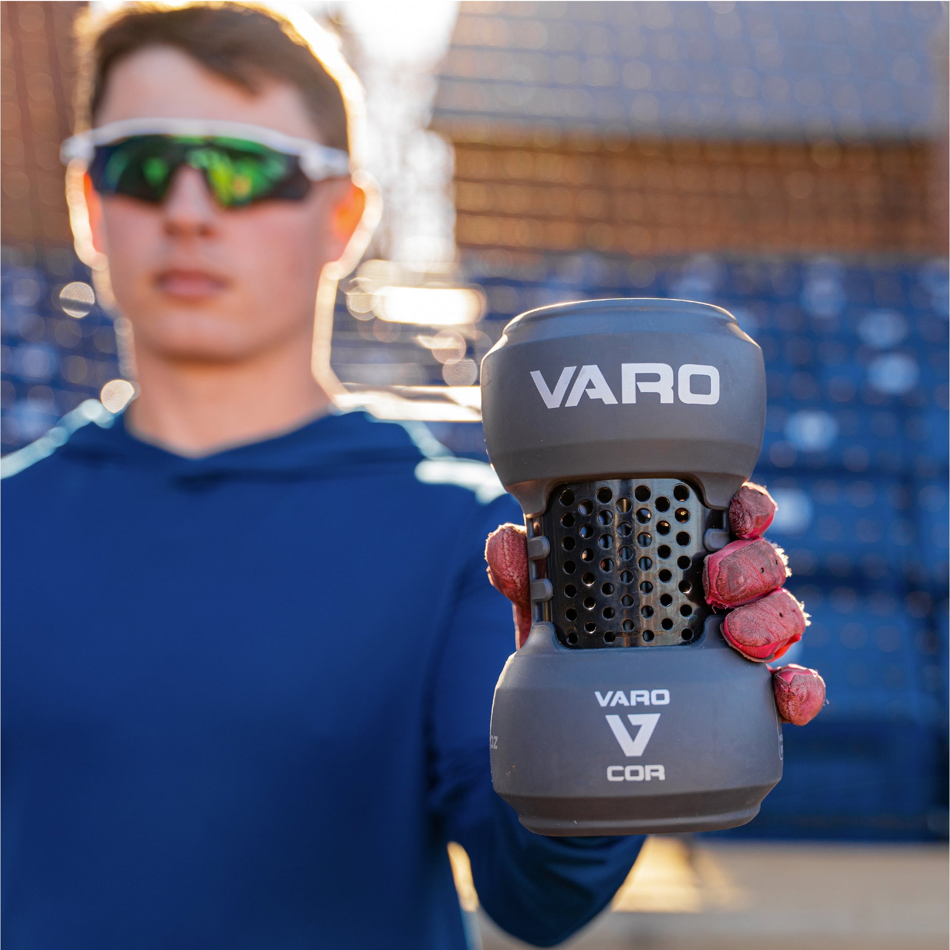 Person holding a Varo COR Bat Training Weight 24oz with a blurred background