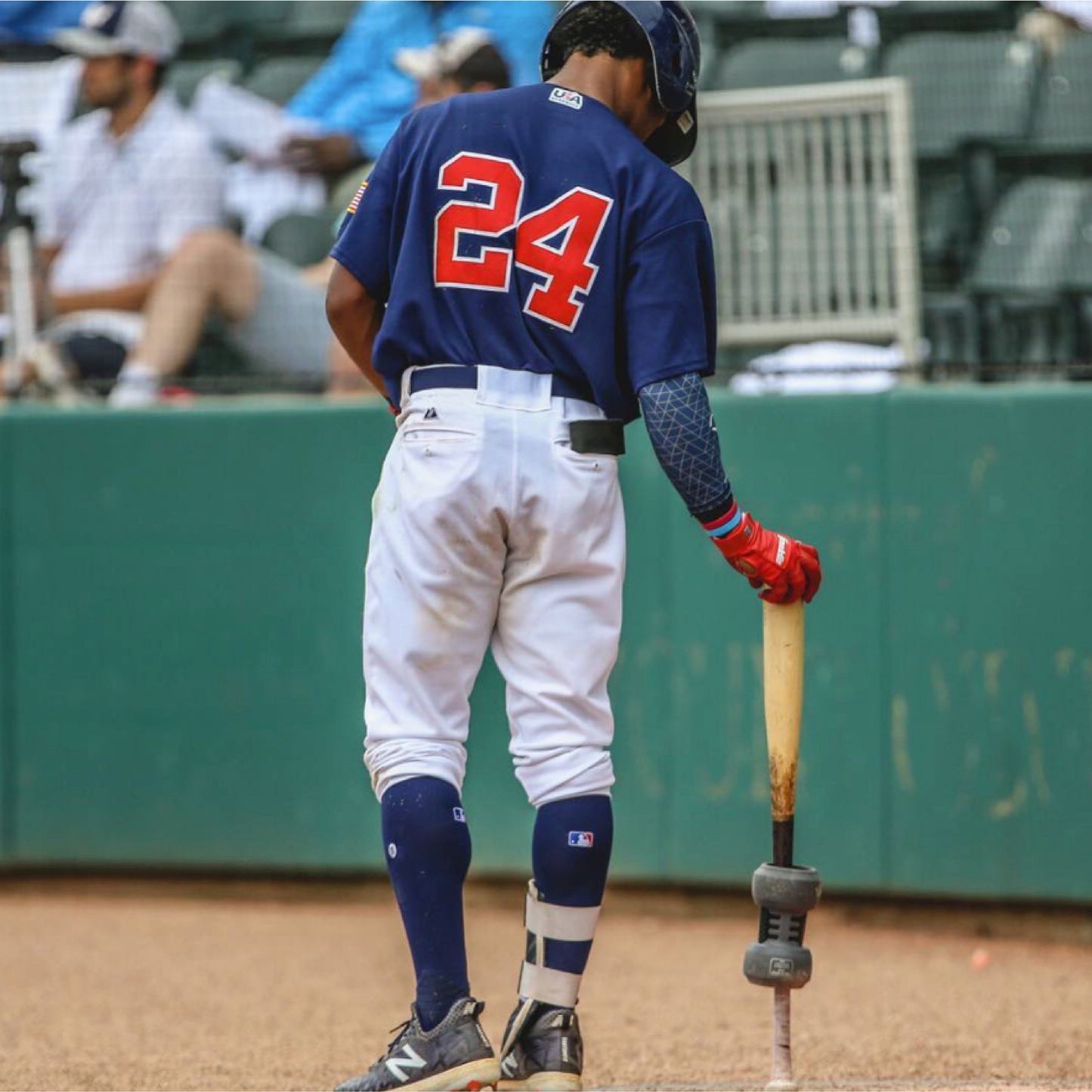 Baseball player in blue uniform with number 24 holding a bat with Varo COR Bat Training Weight 24oz attached on it, on a baseball field.