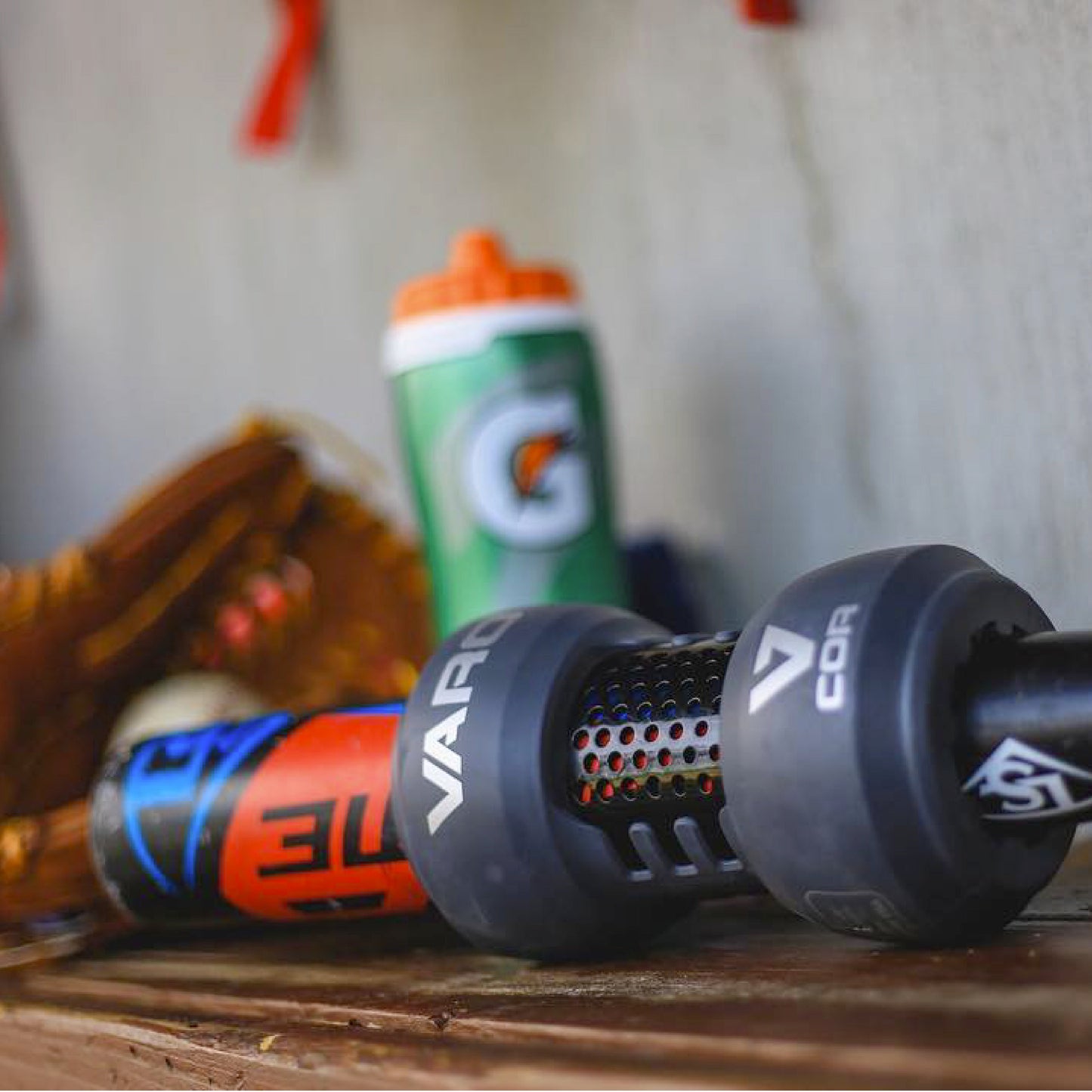 Close-up of workout equipment including a baseball bat with Varo COR Bat Training Weight 20oz attached on it, on a wooden surface.